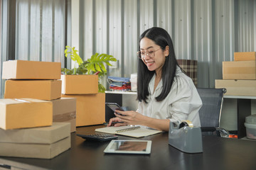 Young business woman working online e-commerce shopping at her shop. Young woman seller prepare...