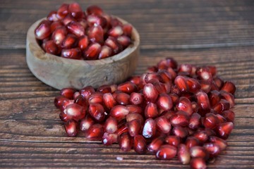 red pomegranate seeds in a wooden bowl and on a wooden table