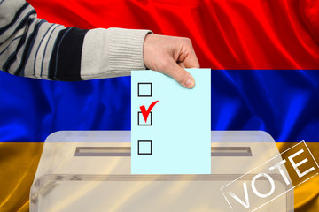 Fototapeta na wymiar male voter drops a ballot in a transparent ballot box against the background of the national flag of Armenia, concept of state elections, referendum