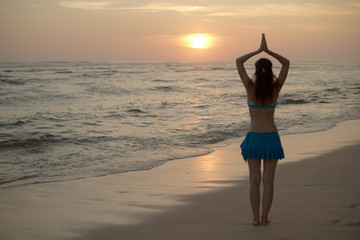 Yoga pose. Woman standing on the beach, practicing yoga. Young woman raising arms with namaste...