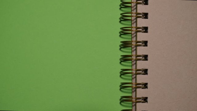 Turning page of brown ringbinder sketchbook revealing green screen