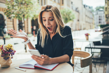 Happy Caucasian female surprised with received promotion advertising with discount for web shopping, amazed hipster girl shocked with high speed internet connection on modern cellular technology