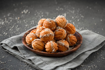 homemade cookies in the form of nuts with a filling boiled condensed milk stacked in a pyramid in a wooden plate on a gray background