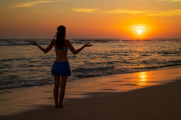 Yoga pose. Woman standing on the beach, practicing yoga. Young woman raising arms with gyan mudra...