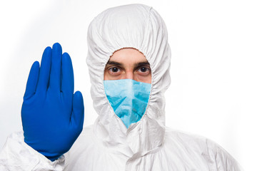 Portrait of young man in protective white medical uniform giving STOP sign during coronavirus pandemic. Epidemic, pandemic of coronavirus covid 19.