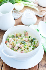 Traditional summer okroshka soup with sausage in a white bowl, selective focus