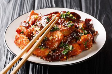 Spicy stir fried mala chicken with the addition of sesame seeds and greens closeup in a plate. horizontal