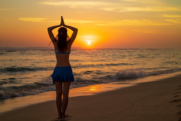 Yoga pose. Woman standing on the beach, practicing yoga. Young woman raising arms with namaste...
