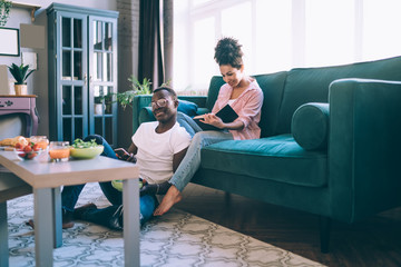 Smiling multiracial couple relaxing with smartphone and book at home