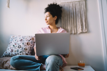 Relaxed ethnic woman browsing laptop and resting at home