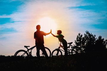 Silhouette of happy father and son biking at sunset