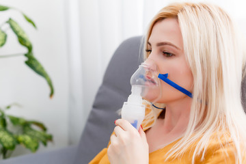 woman makes inhalation nebulizer at home. holding a mask nebulizer inhaling fumes spray the medication into your lungs sick patient. self-treatment of the respiratory tract using inhalation nebulizer