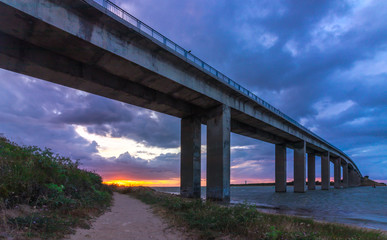 Low sunset under the bridge to Noirmoutier, France, with dramatic purple clouds