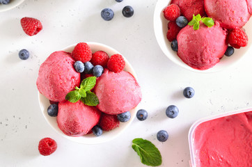 Raspberry ice cream scoop with fresh raspberries and blueberries in bowl