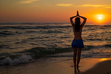 Yoga pose. Woman standing on the beach, practicing yoga. Young woman raising arms with namaste...