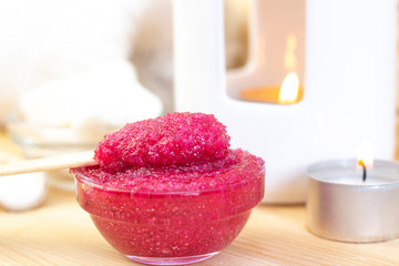 Obraz na płótnie Canvas Natural pink body scrub made from sugar. Pink scrub in a glass cup on a background of candles and sugar.