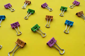 Multicolored smiley paper clips lie on a bright yellow background