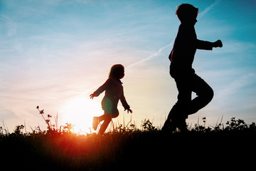 Silhouette of happy boy and girl running at sunset