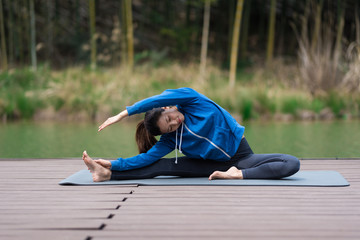 A young Asian woman doing yoga by the lake