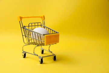 One chicken egg in grocery cart on a yellow background