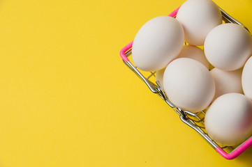 Chicken eggs in a metal grocery basket on a yellow background