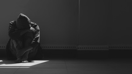 Sunlight and shadow on surface of hopeless man sitting alone with hugging his knees on the floor in empty dark room in black and white style