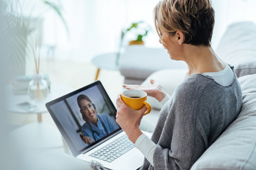 Woman using laptop and having video call with her doctor while sitting at home. - obrazy, fototapety, plakaty