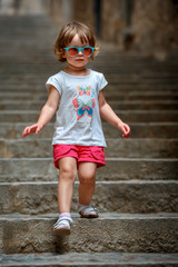 Cute curly toddler girl walking in famous ancient medieval city Girona, Catalonia, Spain