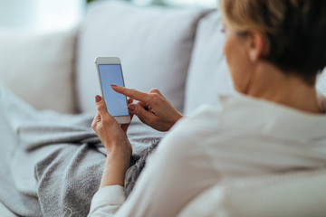 Close-up of woman texting on mobile phone while relaxing on the sofa.