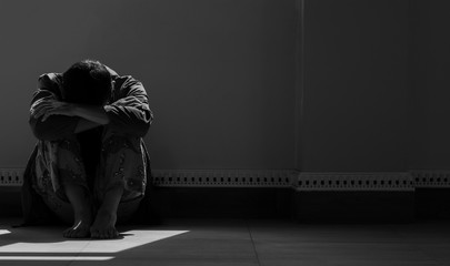 Sunlight and shadow on surface of hopeless man sitting alone with hugging his knees on the floor in empty dark room in black and white style - obrazy, fototapety, plakaty