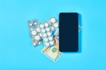 Smartphone near pills and banknote of one hundred dollars on blue background. E-health, e-medicine, payment for services concept. Online purchasing, consultation, medical assistance