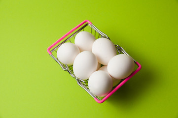 Eggs in a metal grocery basket on a neon green background