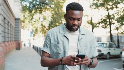 Handsome stylish african american young attractive man using phone walk on street smile sunlight sunset cellphone fashion internet face outside technology businessmen black young city mobile close up