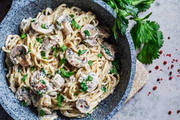 Creamy mushroom spaghetti pasta with parsley in gray pan, gray background.