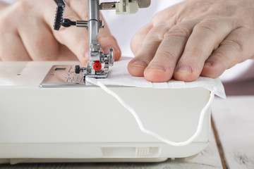 disposable face shield and homemade multi-face mask lie on the sewing machine, blue background, make yourself a protective mask from the fabric at home, do-it-yourself protective mask