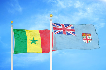 Senegal and Fiji two flags on flagpoles and blue cloudy sky