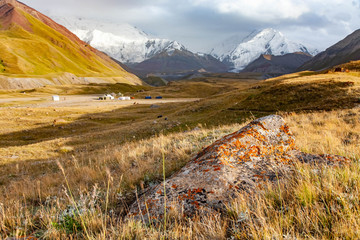 Stone with orange moss and lichen on foreground. Snowy mountains. Beautiful landscape of Kyrgyz...