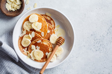 Traditional pancakes with banana, almonds and honey in white plate, top view.