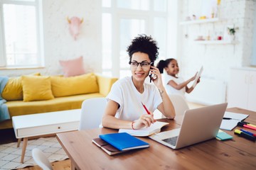 Cheerful black parent answering call near child