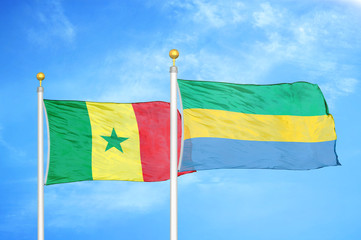 Senegal and Gabon two flags on flagpoles and blue cloudy sky