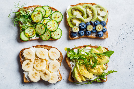 Breakfast toasts with various healthy toppings. Sandwiches  with cream cheese, fruits, berries and honey, salted toasts with avocado and cucumber, top view.