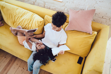 Joyful girl with mother cuddling on soft couch and reading book