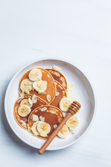 Pancakes with banana, almonds and honey in white plate, top view.