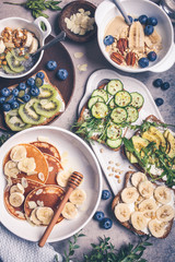 Healthy vegetarian breakfast, flat lay. Oatmeal with fruits, chia pudding, pancakes with banana and honey and toasts with fruits, vegetables and cream cheese.