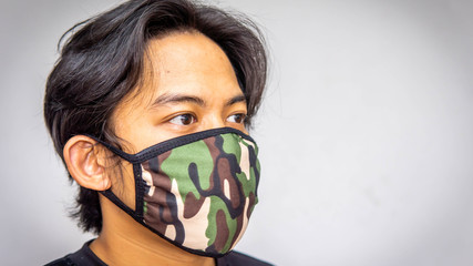 A portrait of a young Malay man wearing an army camouflage face mask on isolated white background.
