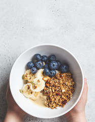 Granola with berries and fruits in a white bowl in hands. Healthy breakfast concept.