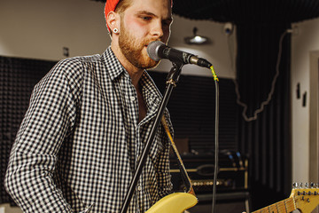 awesome caucasian musician play electric guitar and sing in recording studio. man preparing, practicing before music performance, before concert. music, instruments concept