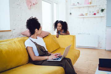 Black woman working on laptop with daughter telling joke