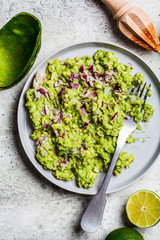 Cooking Guacamole - avocado dip with red onion in gray plate with ingredients, top view.