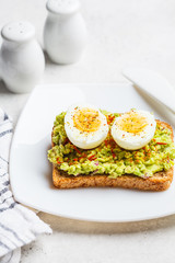 Breakfast avocado toast with egg on a white plate.